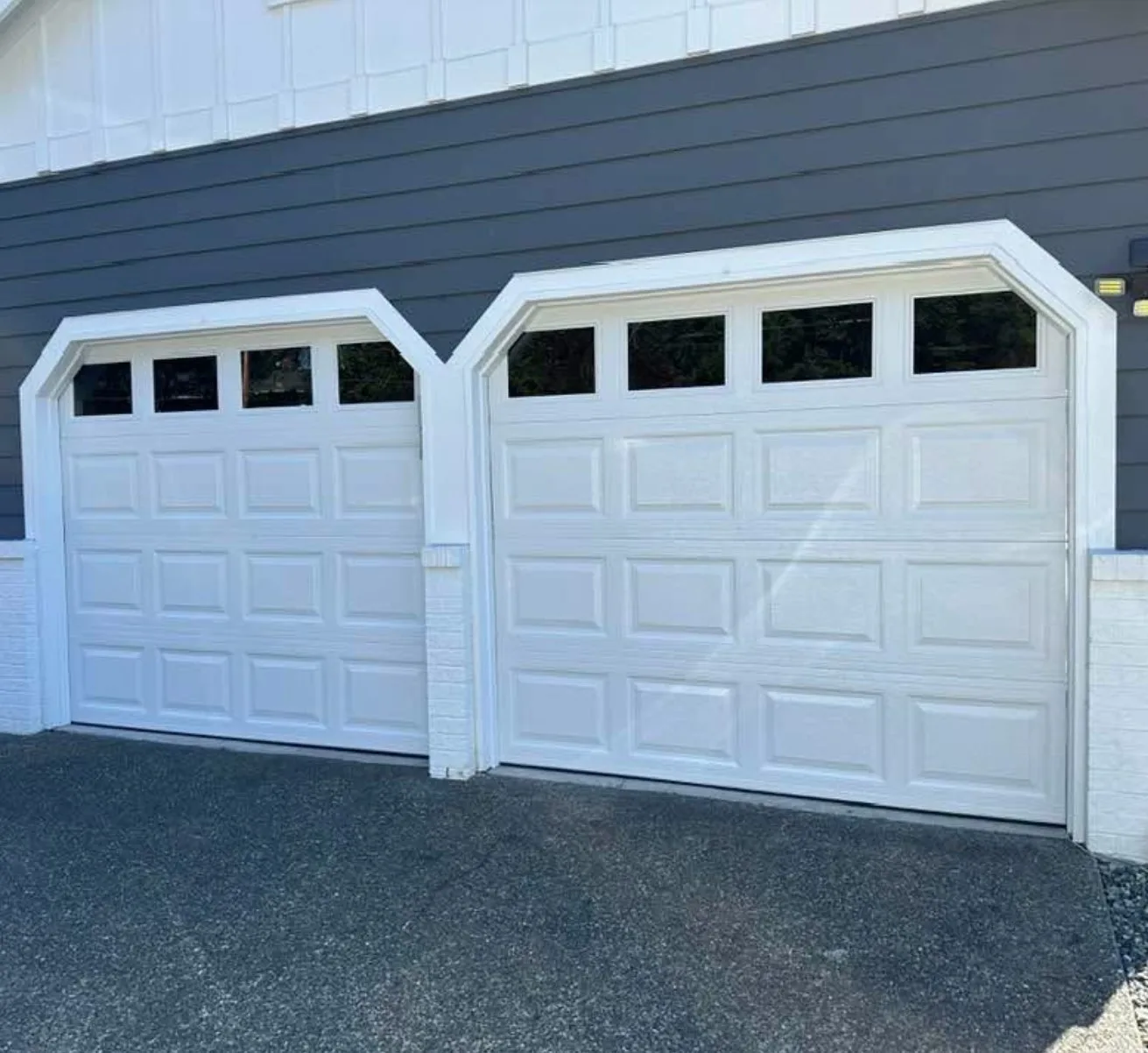 Two white garage doors with windows side by side on a blue house.