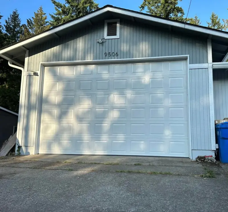 A white raised-panel garage door on a pale blue house.