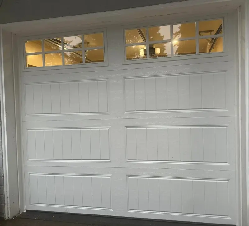 A white stamped-panel garage door with a row of windows, seen from inside the garage.