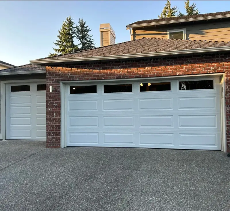 A white long-panel garage door with a row of windows on a brick house.