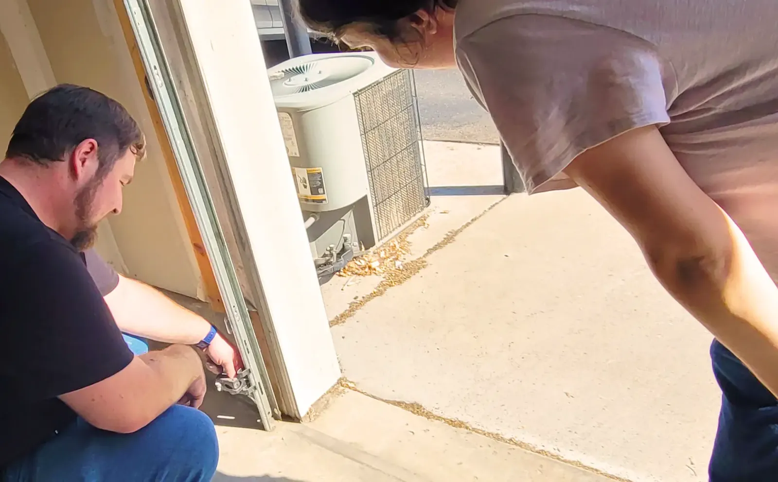 Peter kneeling to check a garage door safety sensor while the homeowner watches.