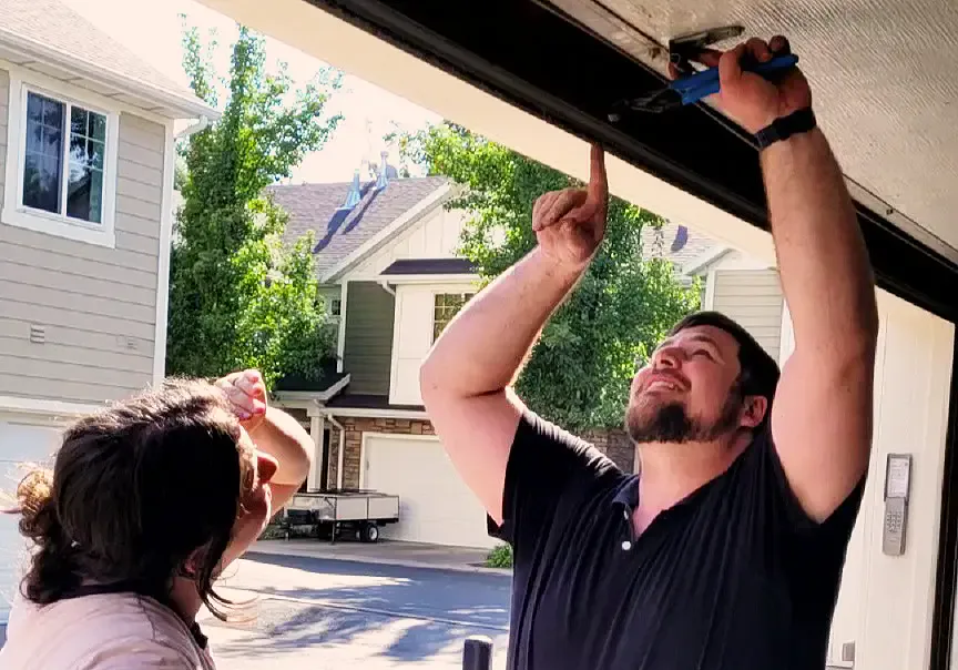 Peter pointing out the torsion spring above an open garage door while a customer looks on.