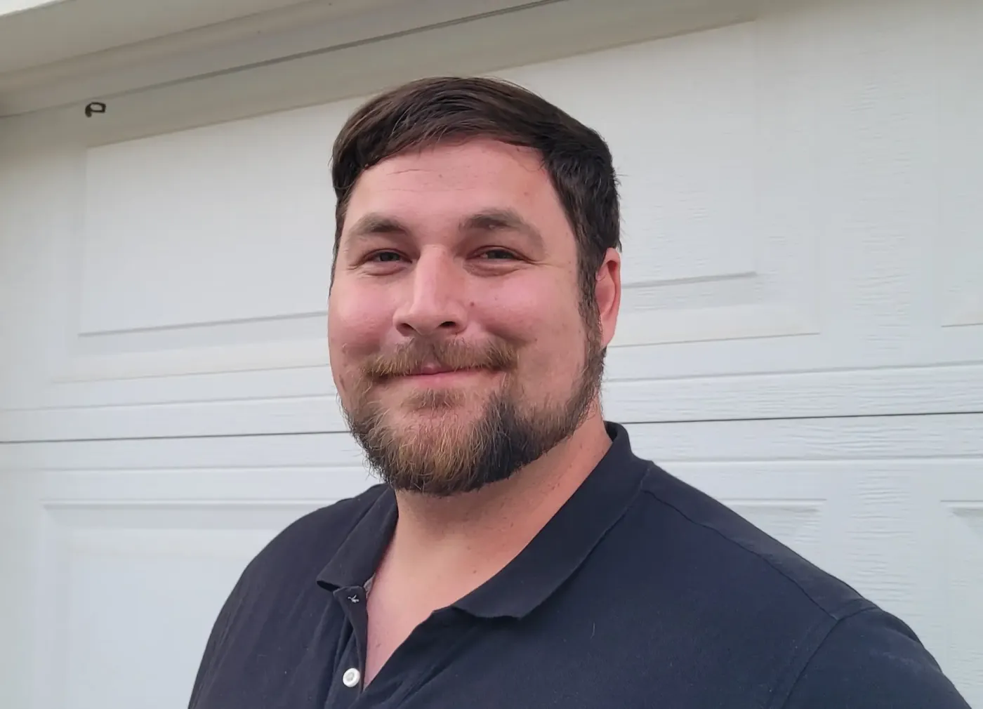 Peter, owner of Trusted Garage Door, smiling in front of a white garage door.