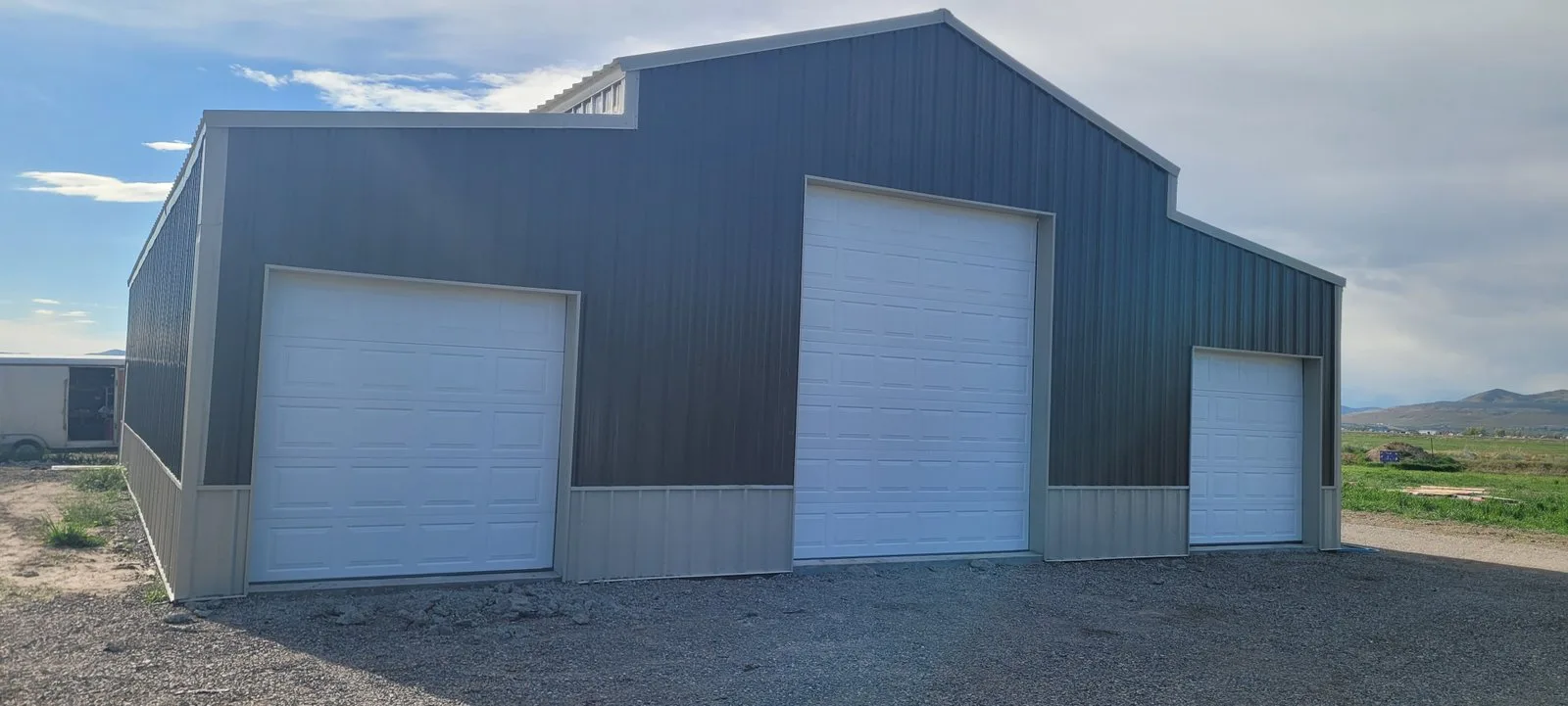 A new navy steel shop building with three white overhead doors under a wide sky.